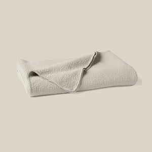 A folded light beige textured blanket or throw, shown on a solid light beige background. - Number 1