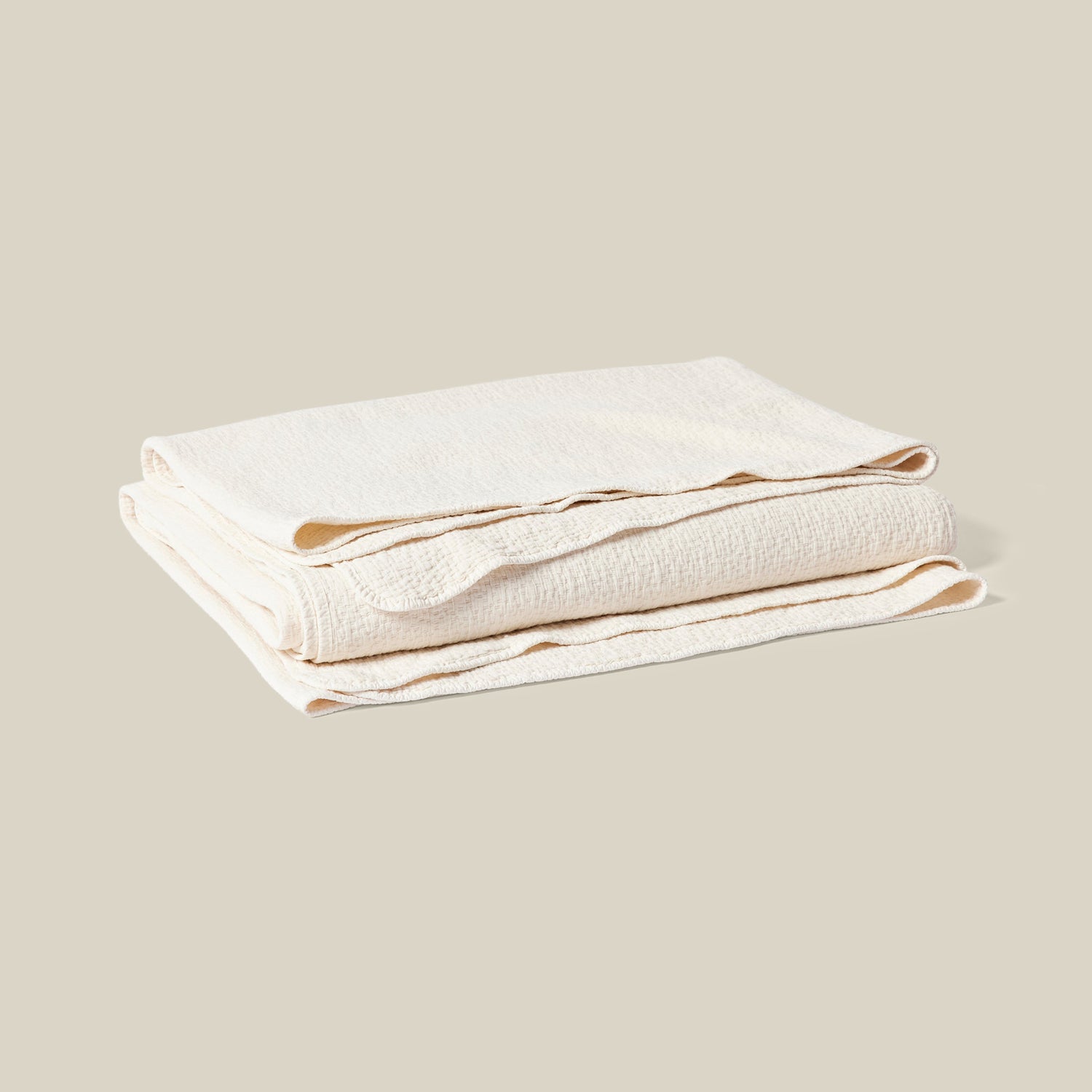 A folded cream-colored textured blanket or throw, shown on a solid light beige background.- Number 1