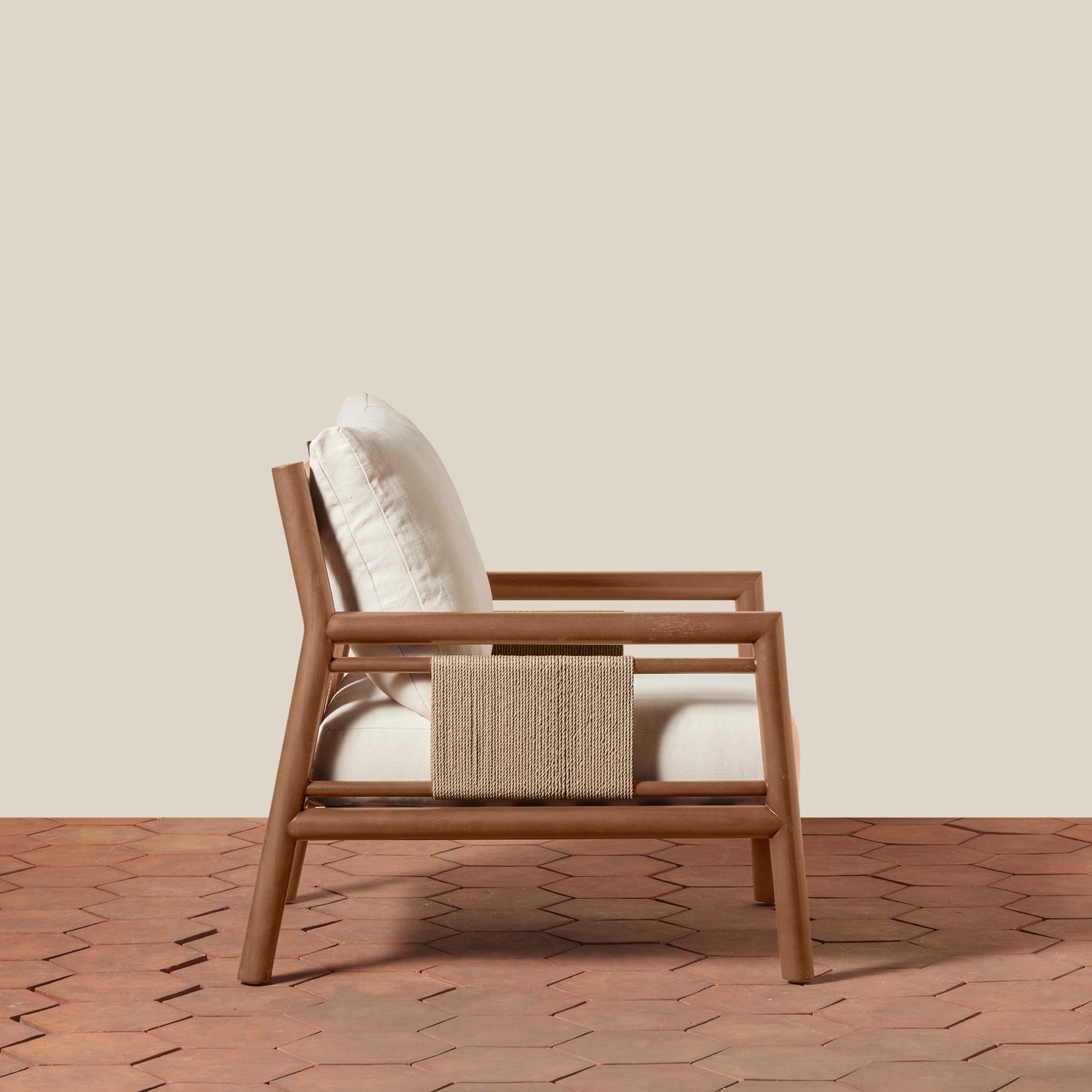 A modern wooden armchair with white cushions and a woven beige accent, set against a solid beige wall and a terracotta hexagonal tile floor.- Number 3