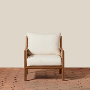 A modern armchair with a warm brown frame and thick off-white cushions, set against a solid beige wall and a terracotta hexagonal tile floor. - Number 4