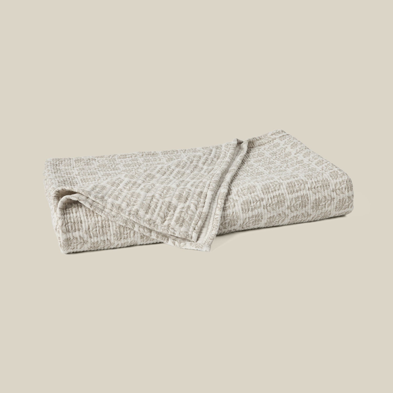 A folded textured blanket in a light beige and gray heathered pattern, set against a solid beige background.- Number 1