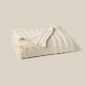 A folded cream-colored textured blanket with a ribbed pattern and fringed edges, displayed on a solid light beige background. - Number 1