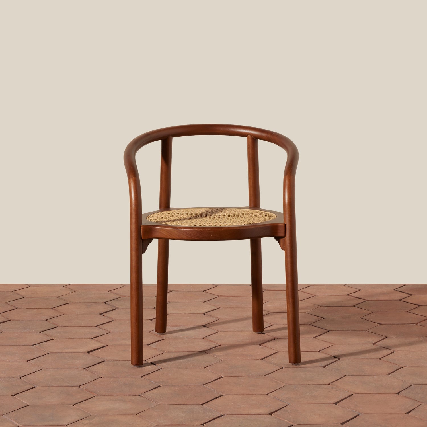 A bentwood dining chair with a warm brown wood frame and a natural woven cane seat, positioned against a neutral beige wall and terracotta hexagonal tile floor.- Number 9