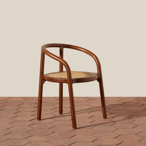 A mid-century modern wooden dining chair with a curved armrest, brown bentwood frame, and a woven cane seat, set against a beige wall and terracotta hexagonal tile floor. - Number 7
