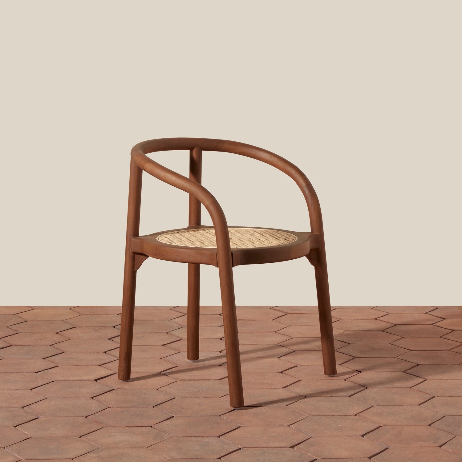 A mid-century modern wooden dining chair with a curved armrest, brown wood frame, and a woven cane seat, set against a beige wall and terracotta hexagonal tile floor.- Number 1
