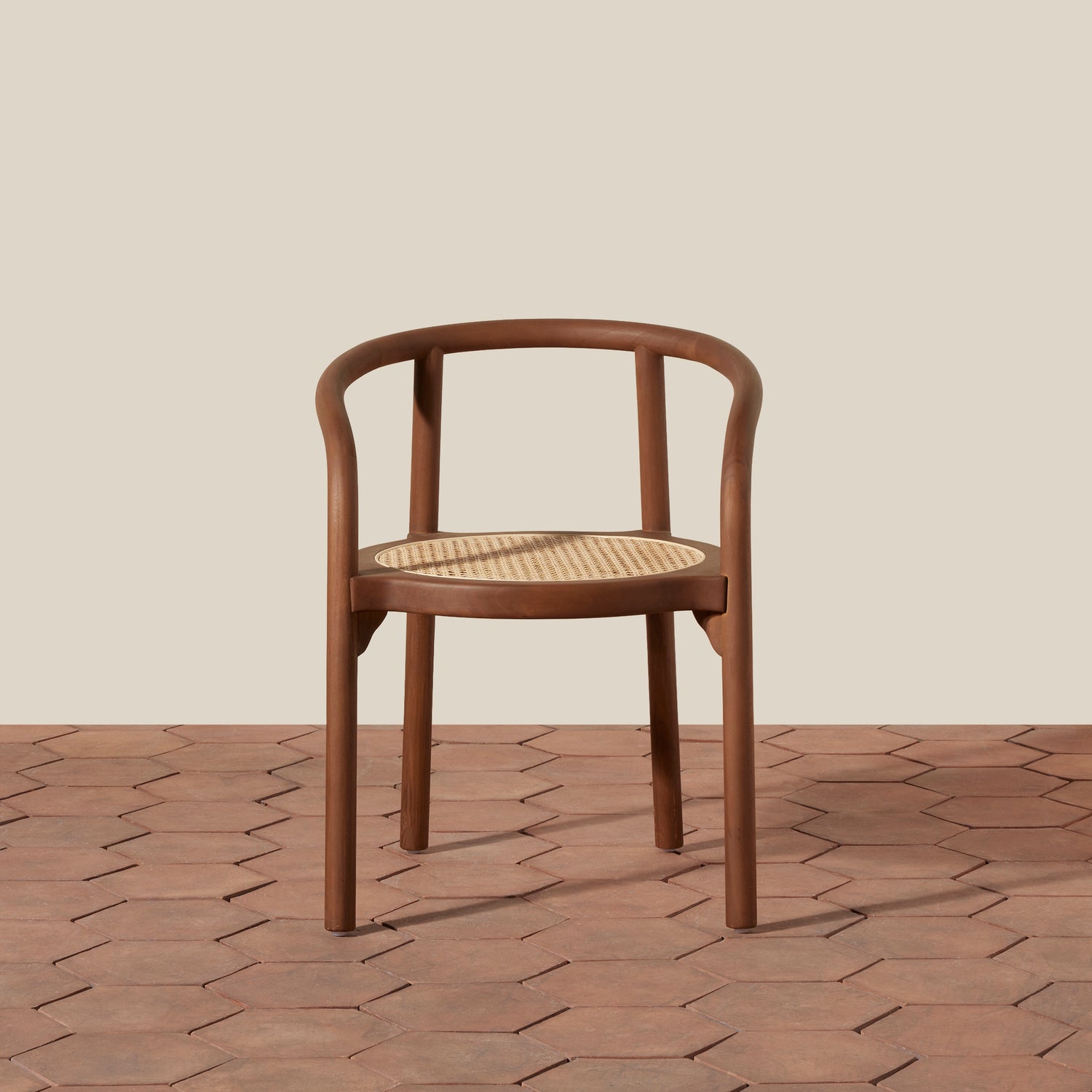 A modern wooden chair with a curved backrest and a woven cane seat, shown on a terracotta hexagonal tile floor against a solid beige background.- Number 3