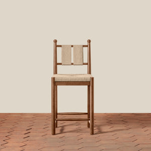 A wooden bar stool with a woven beige seat and backrest, set against a solid beige wall and a terracotta hexagonal tile floor. - Number 4