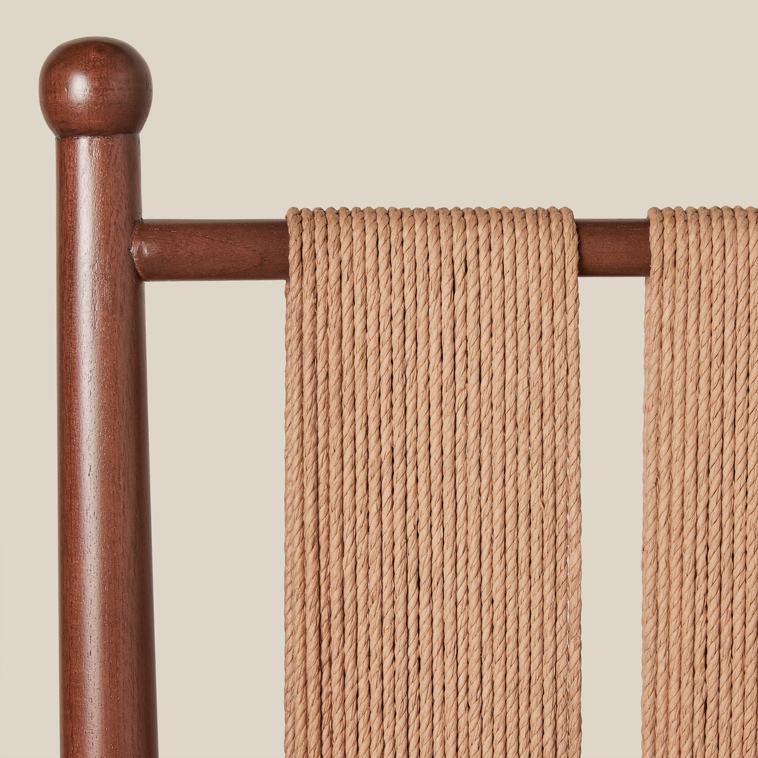 Brown wooden chairback with woven seat rest against a beige background- Number 7