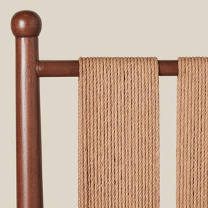 Brown wooden chairback with woven seat rest against a beige background - Number 7