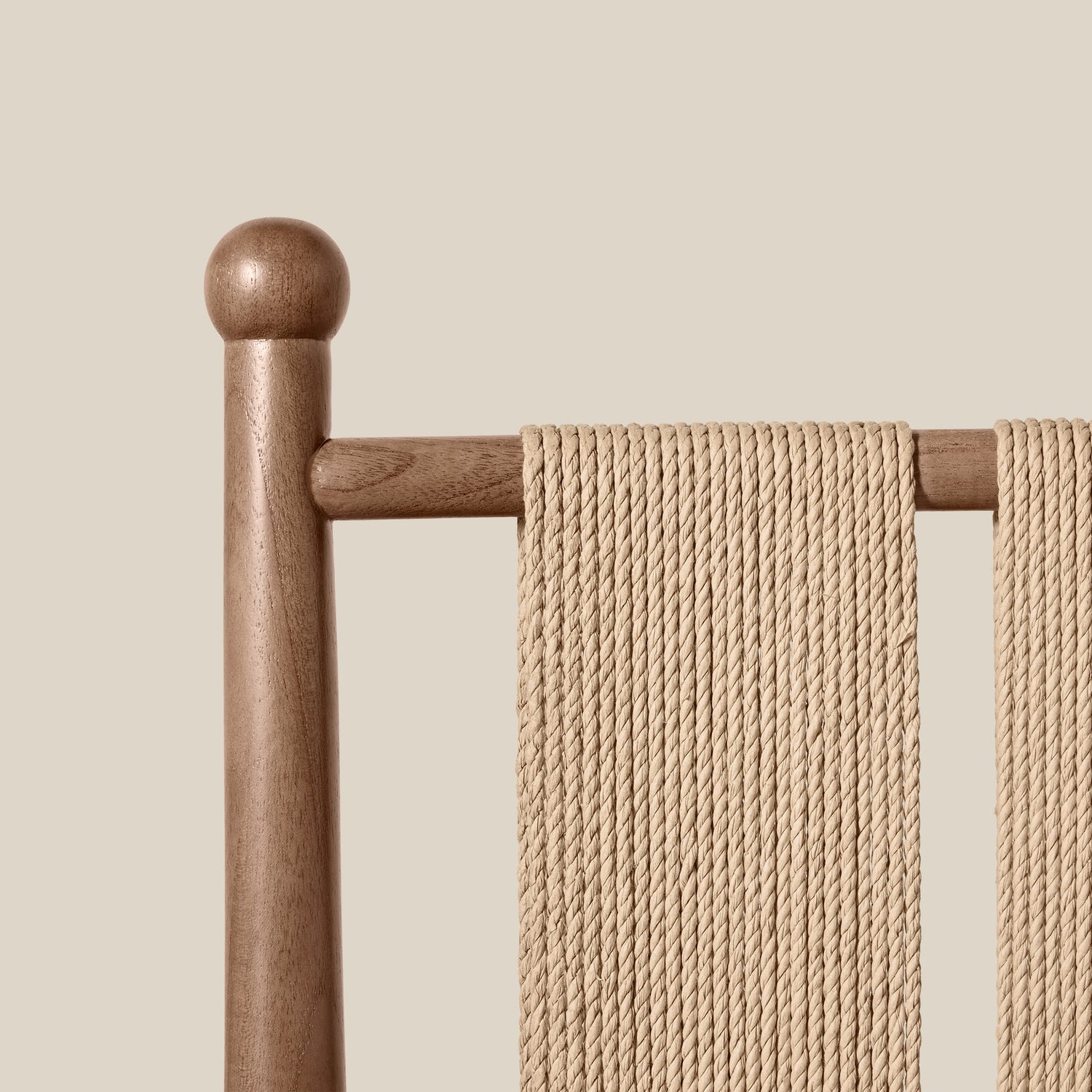 Close-up of a woven rope chair back with a round wooden post and horizontal support bar, shown against a solid light beige background.- Number 15
