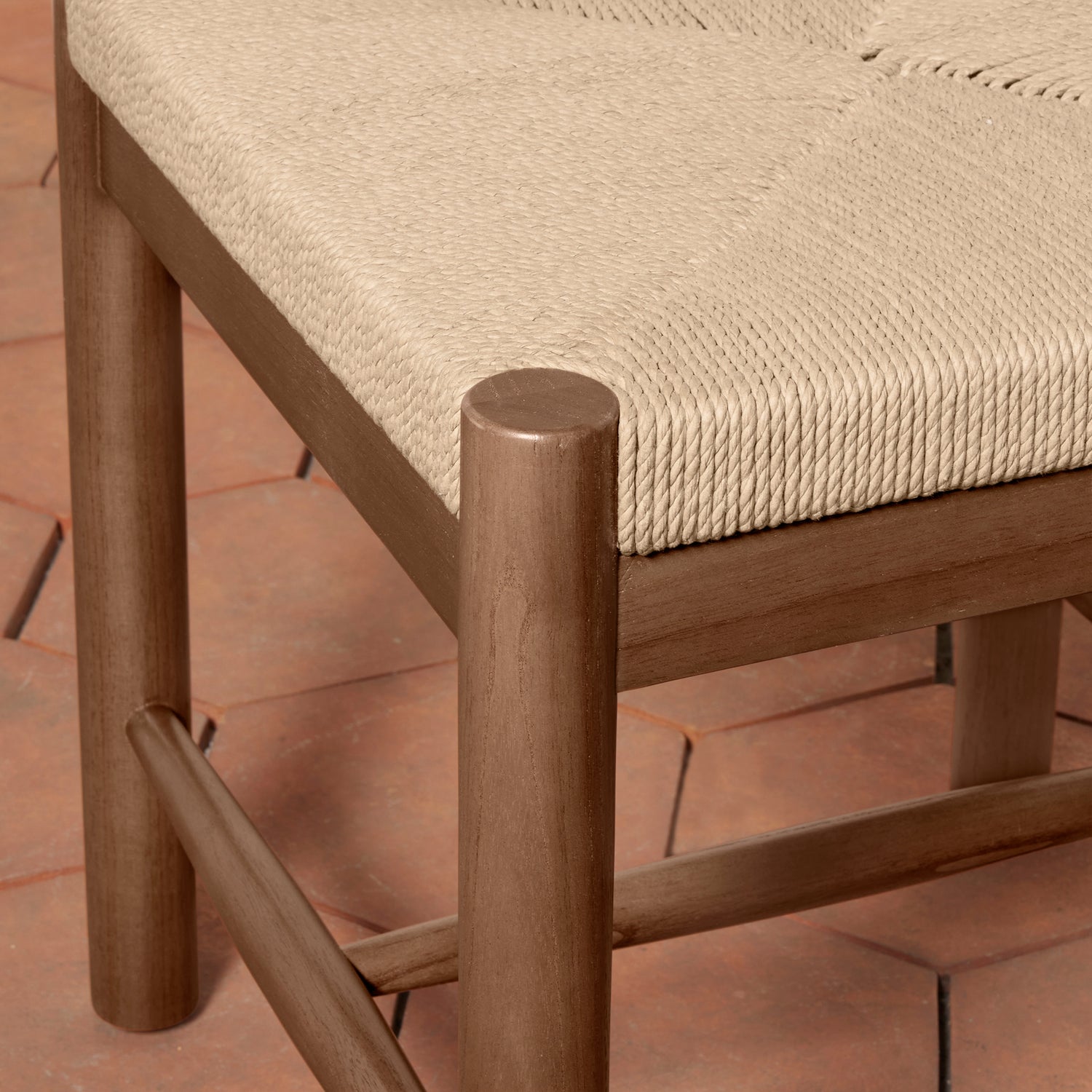 Close-up of a wooden chair with a woven rope seat in a warm beige tone, set on a terracotta tiled floor.- Number 16