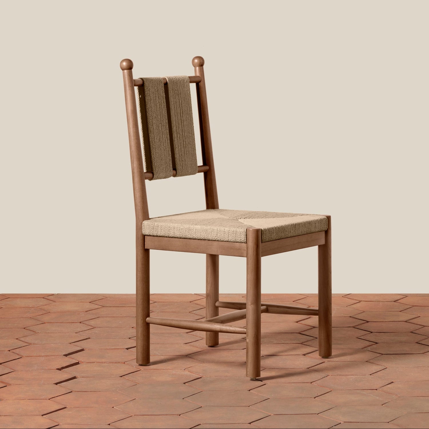 A wooden dining chair with a woven cane backrest and a light beige upholstered seat, set against a solid beige wall and a terracotta hexagonal tile floor.- Number 1