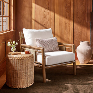 A wooden armchair with white cushions and a small patterned accent pillow, styled in a warm wood-paneled room with a woven side table, vase, and window light. - Number 2