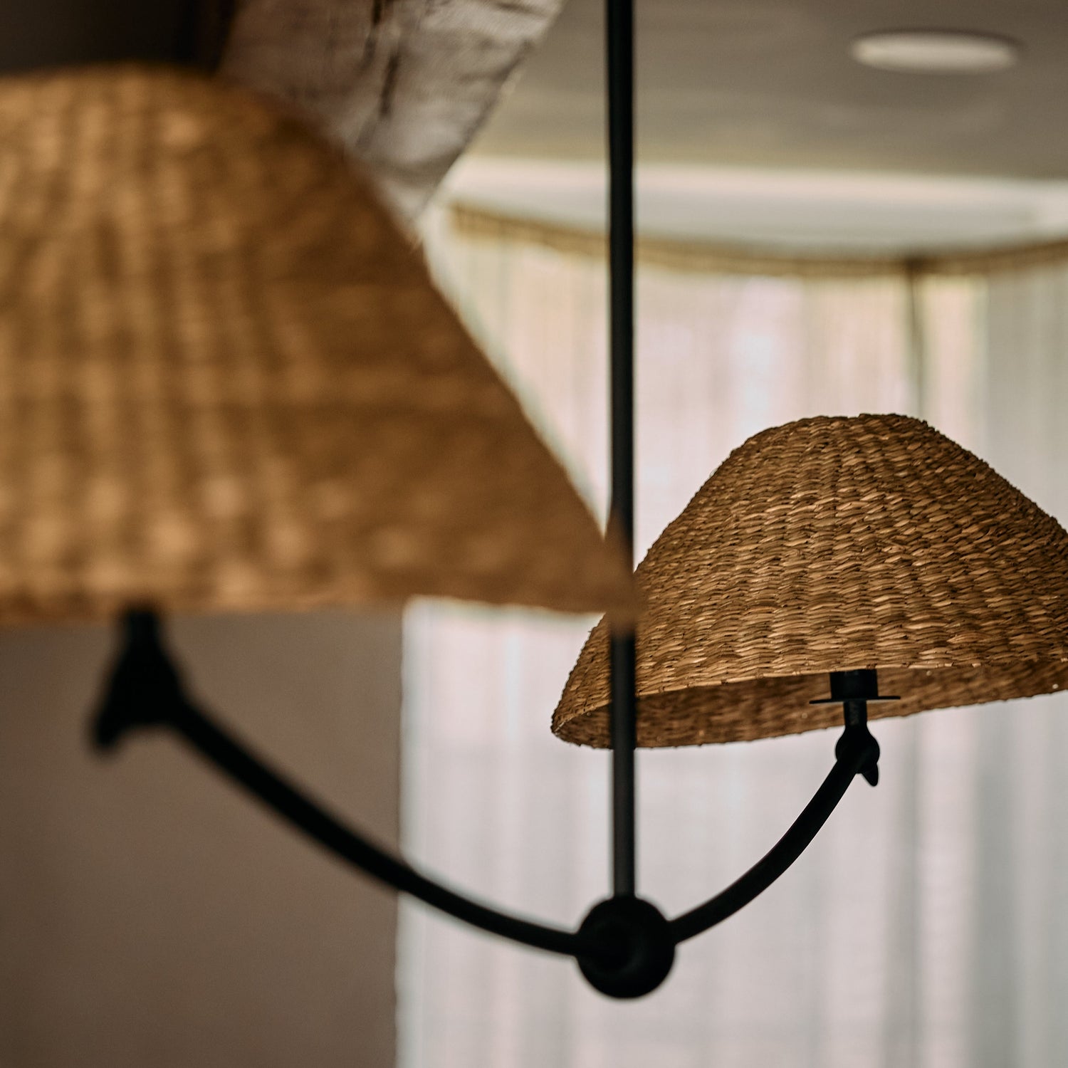 Chandelier with wicker lampshades in a room with light-colored walls and a window.- Number 3