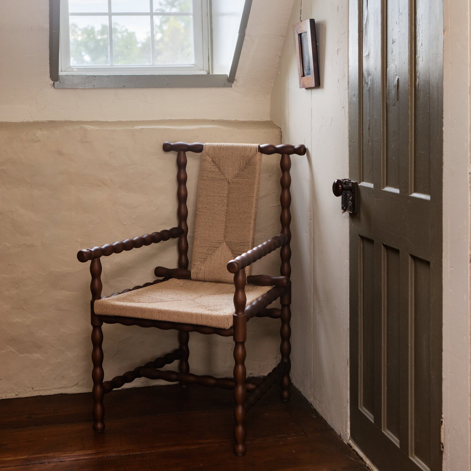 Wooden chair with beige cushion in a room with a window and door.- Number 4