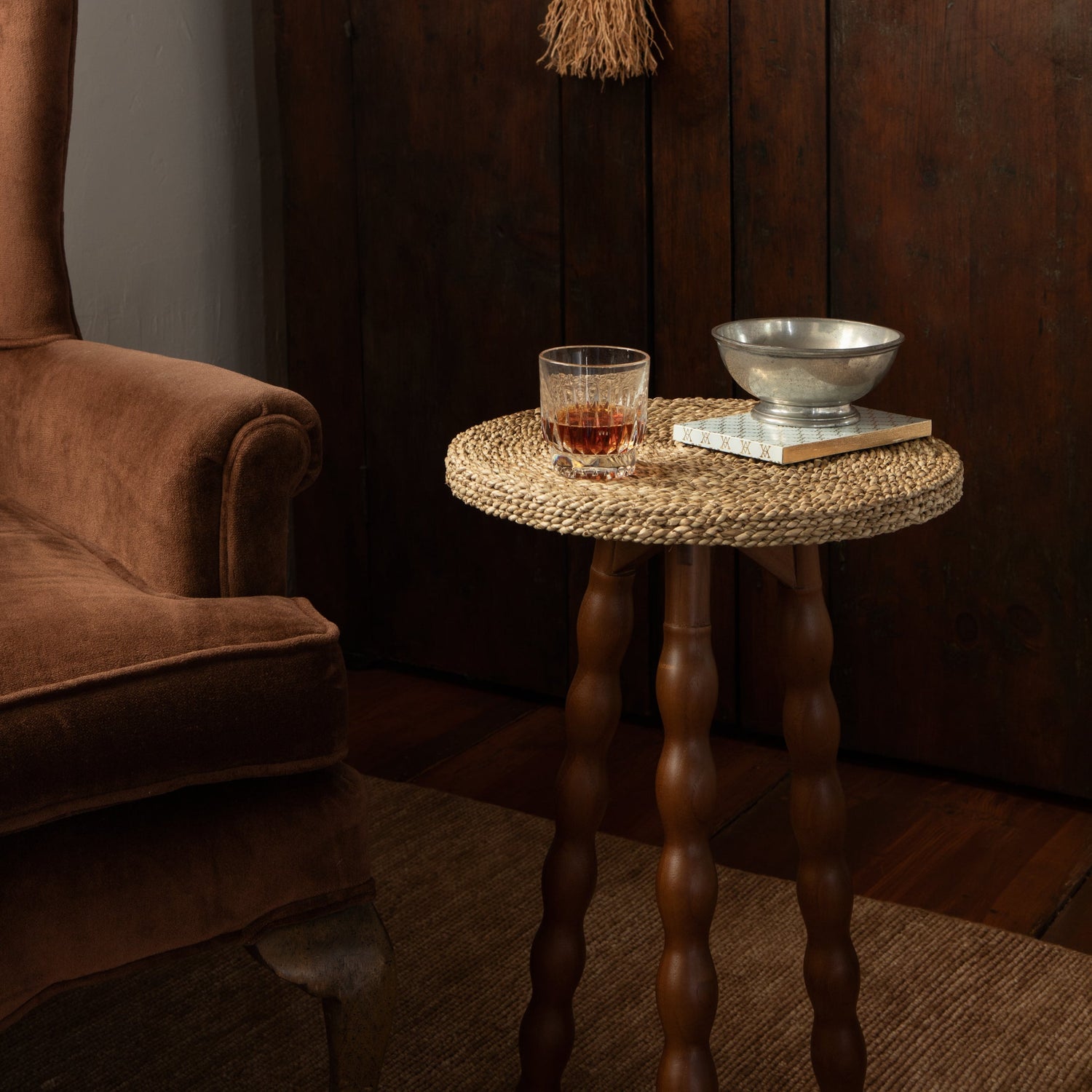 Wooden cabinet with a broom, small table with a glass of whiskey, and a book in a dimly lit room.- Number 3