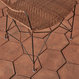 close up of a brown rattan and iron chair seat with pointed legs on tile floor - Number 5
