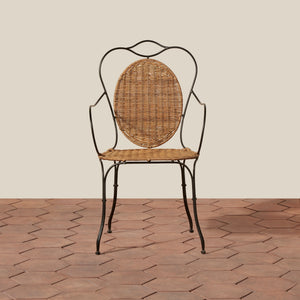 A vintage-style metal and wicker dining chair with a curved black wrought-iron frame, a round woven rattan backrest, and a woven seat, set against a beige wall and terracotta tile floor. - Number 5