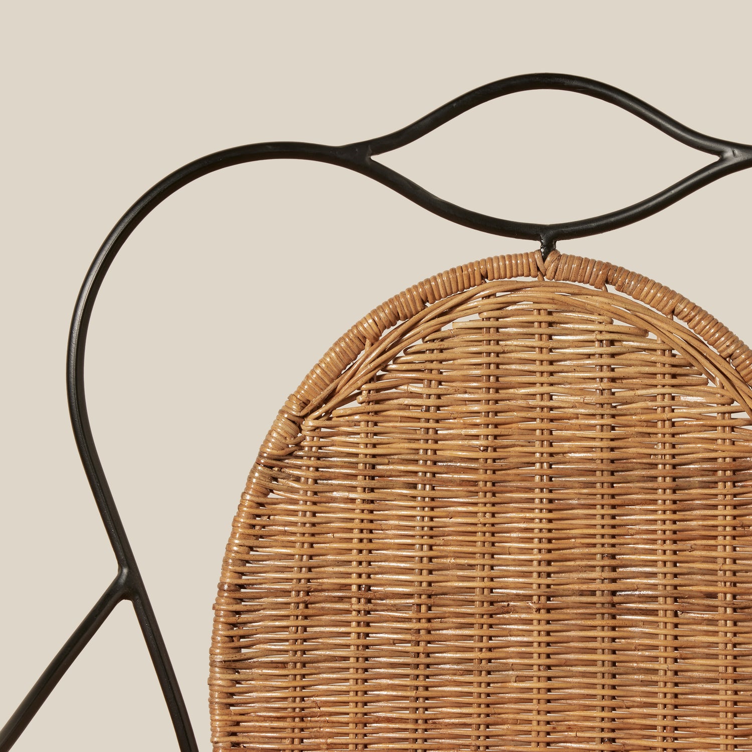 Close-up of a woven rattan chair back with a black metal frame against a solid beige background.- Number 7
