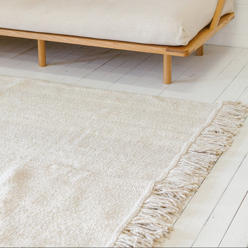 Beige sofa with wooden frame on a light wooden floor with a beige rug.- Number 2