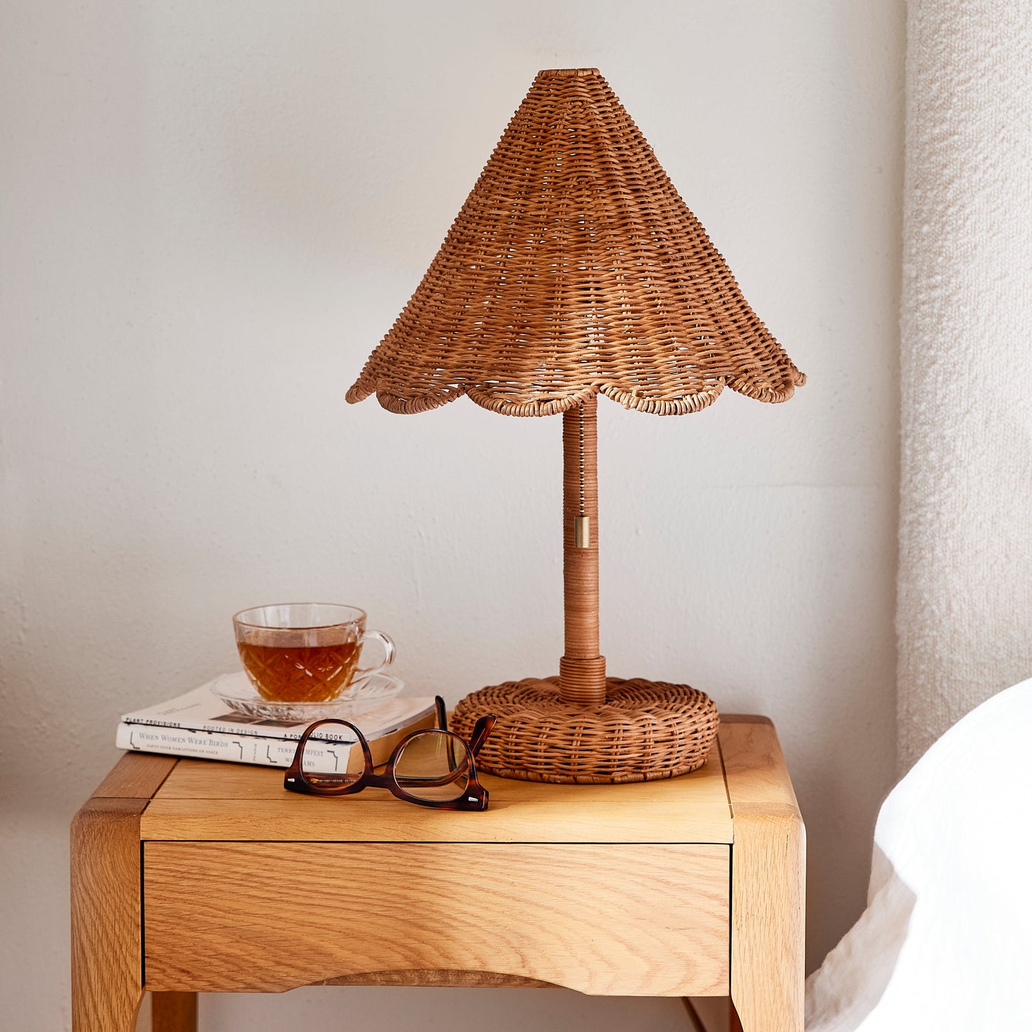Wicker table lamp on a wooden side table with a cup and glasses against a neutral wall.- Number 2