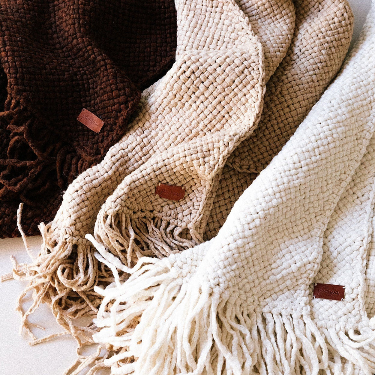 Three woven blankets in brown, beige, and white with fringes on a light background.- Number 5