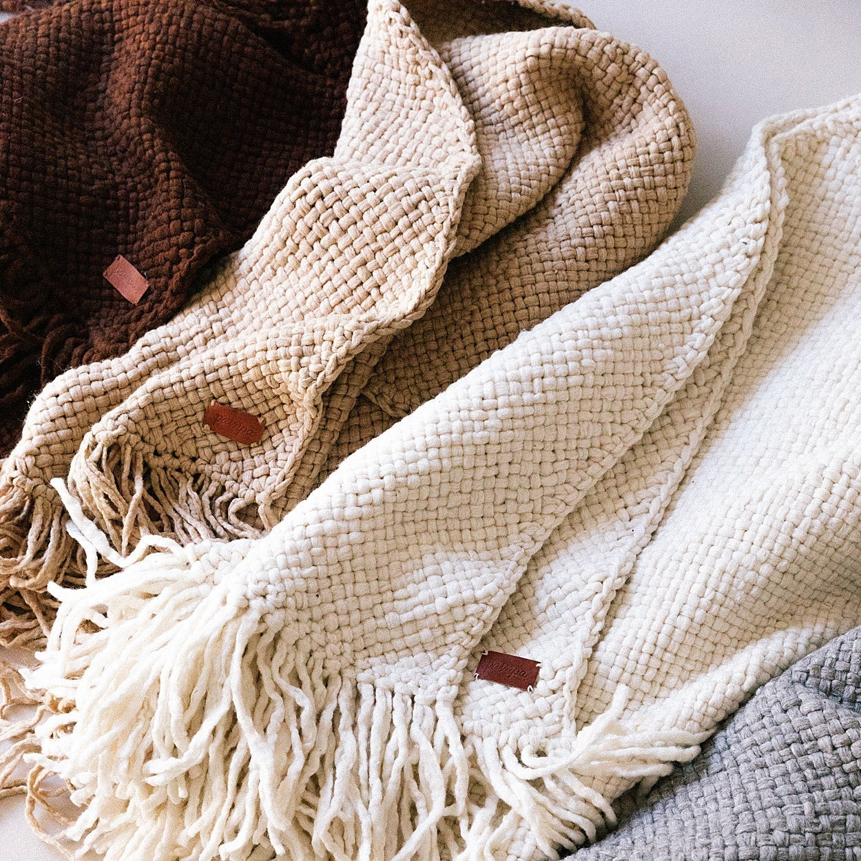 Close-up of textured blankets in beige, brown, and gray with fringes.- Number 5