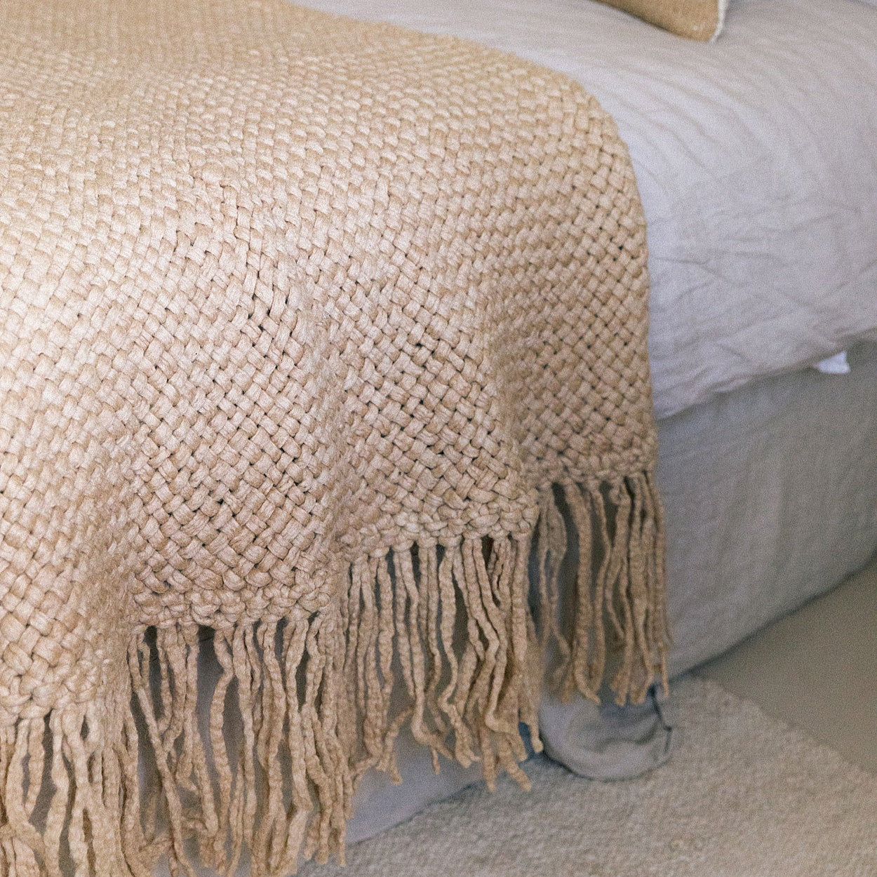 Beige woven blanket with fringes draped over a bed.- Number 2