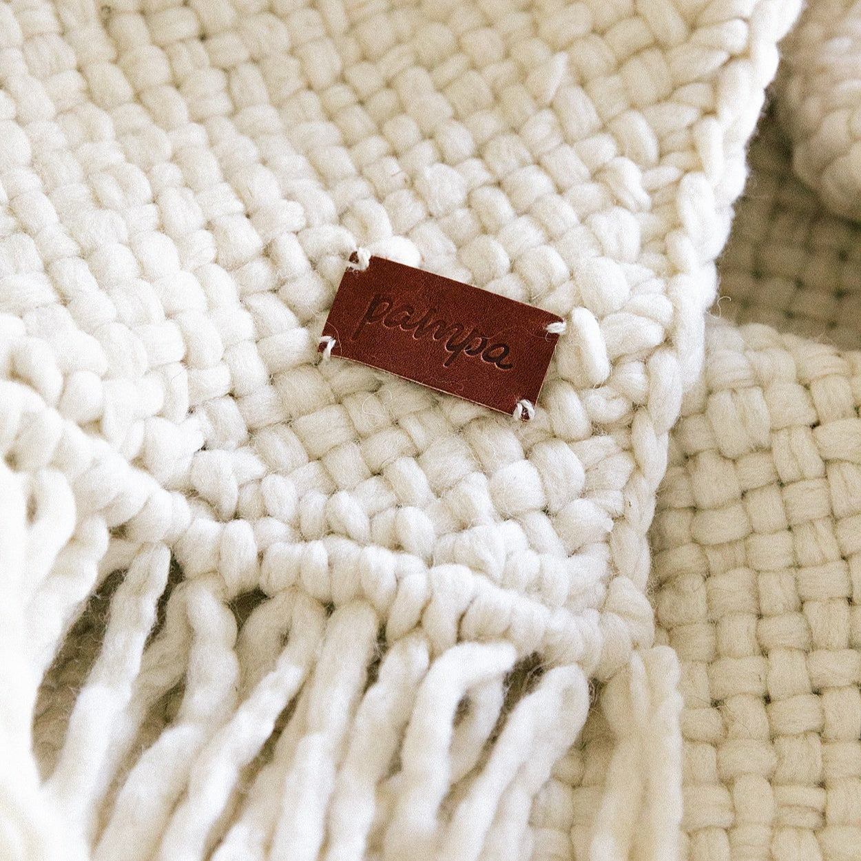 Close-up of a woven beige rug with a leather tag featuring the brand name.- Number 3