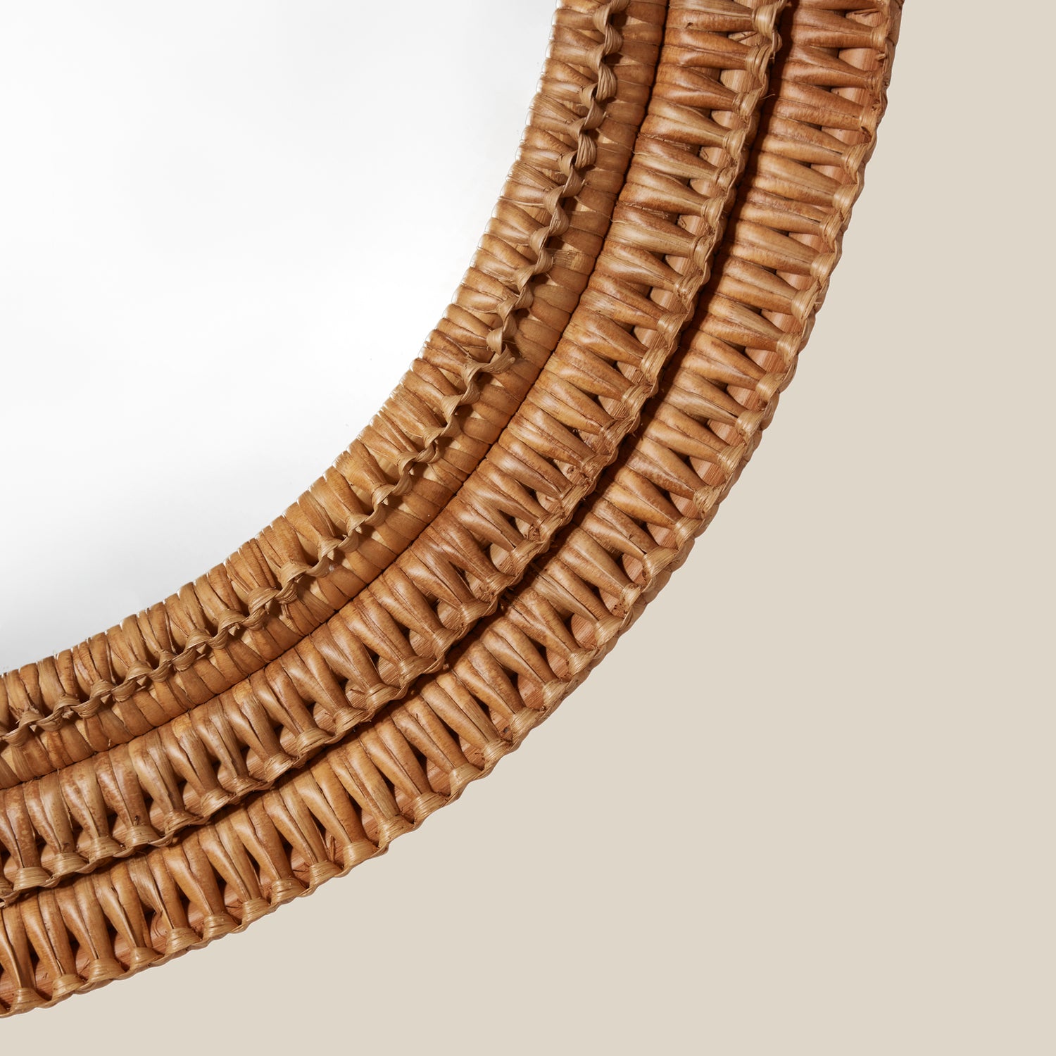 Close up of a round mirror with a woven wicker brown frame on a beige wall- Number 3