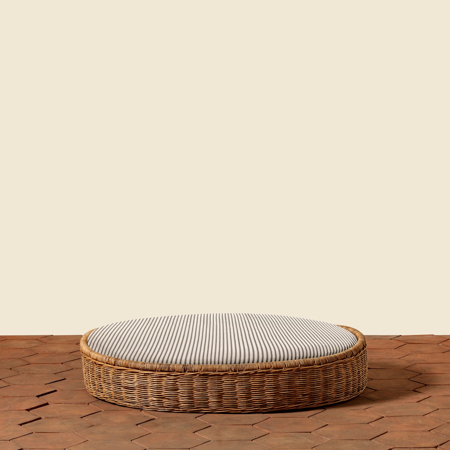 Round wicker ottoman with a striped cushion on a wooden floor.- Number 19