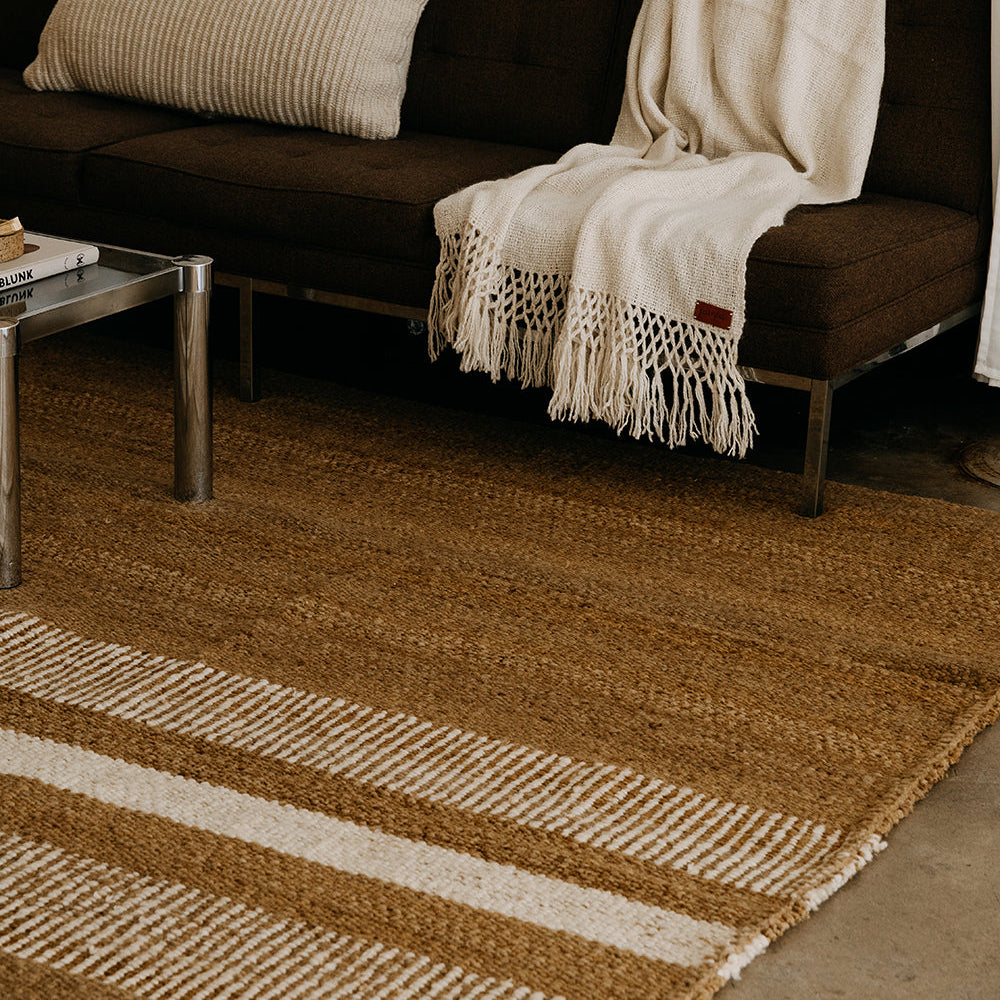 Brown and beige striped rug in front of a dark brown sofa with a white blanket.- Number 3