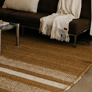 Brown and beige striped rug in front of a dark brown sofa with a white blanket. - Number 3