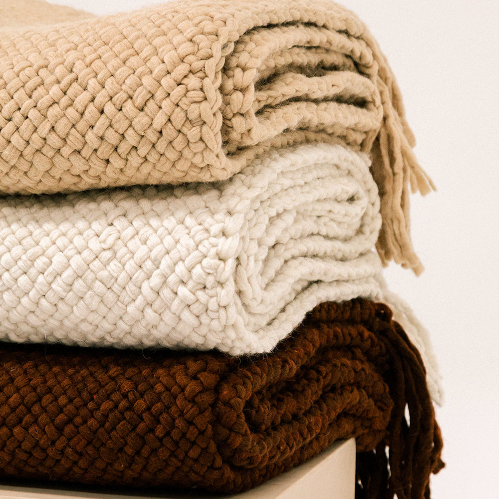 Stack of three folded knit blankets in beige, white, and brown on a light background- Number 6