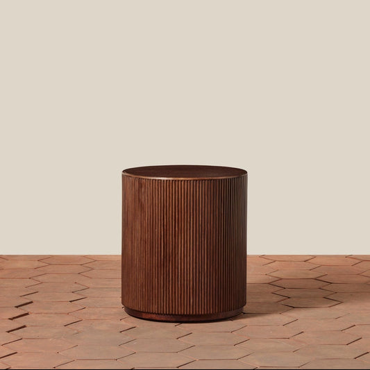 Wooden cylindrical side table on a wooden surface with a beige background