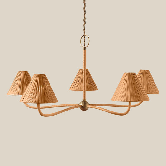 A five-light chandelier with curved brass-toned metal arms and pleated beige fabric shades, suspended from a chain against a solid beige background. - Image 2