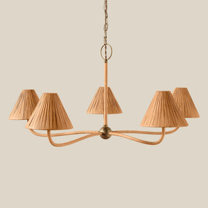 A five-light chandelier with curved brass-toned metal arms and pleated beige fabric shades, suspended from a chain against a solid beige background. - Number 1