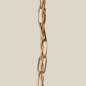 A close-up of a gold-toned chain with elongated oval links and a central twisted rope detail, set against a solid light beige background. - Number 6