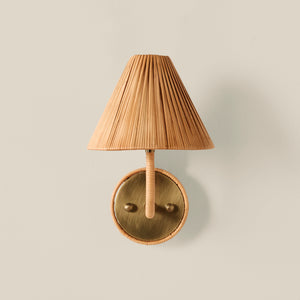 A wall-mounted light fixture with a pleated beige shade, a wrapped beige stem, and a round brass-toned metal backplate, shown against a plain light beige wall. - Number 1