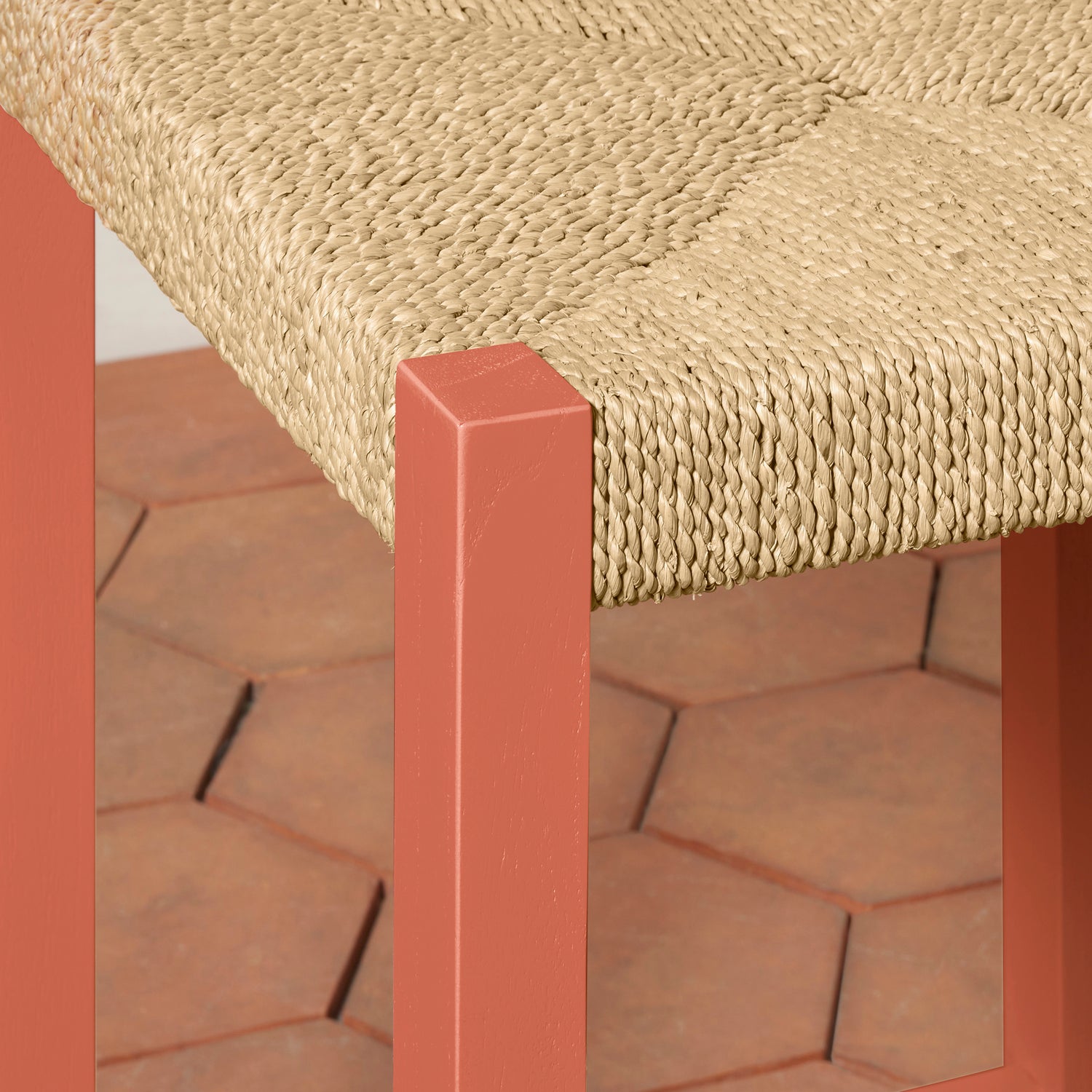 Close-up of a woven chair seat with a red frame on a brick patio.- Number 6