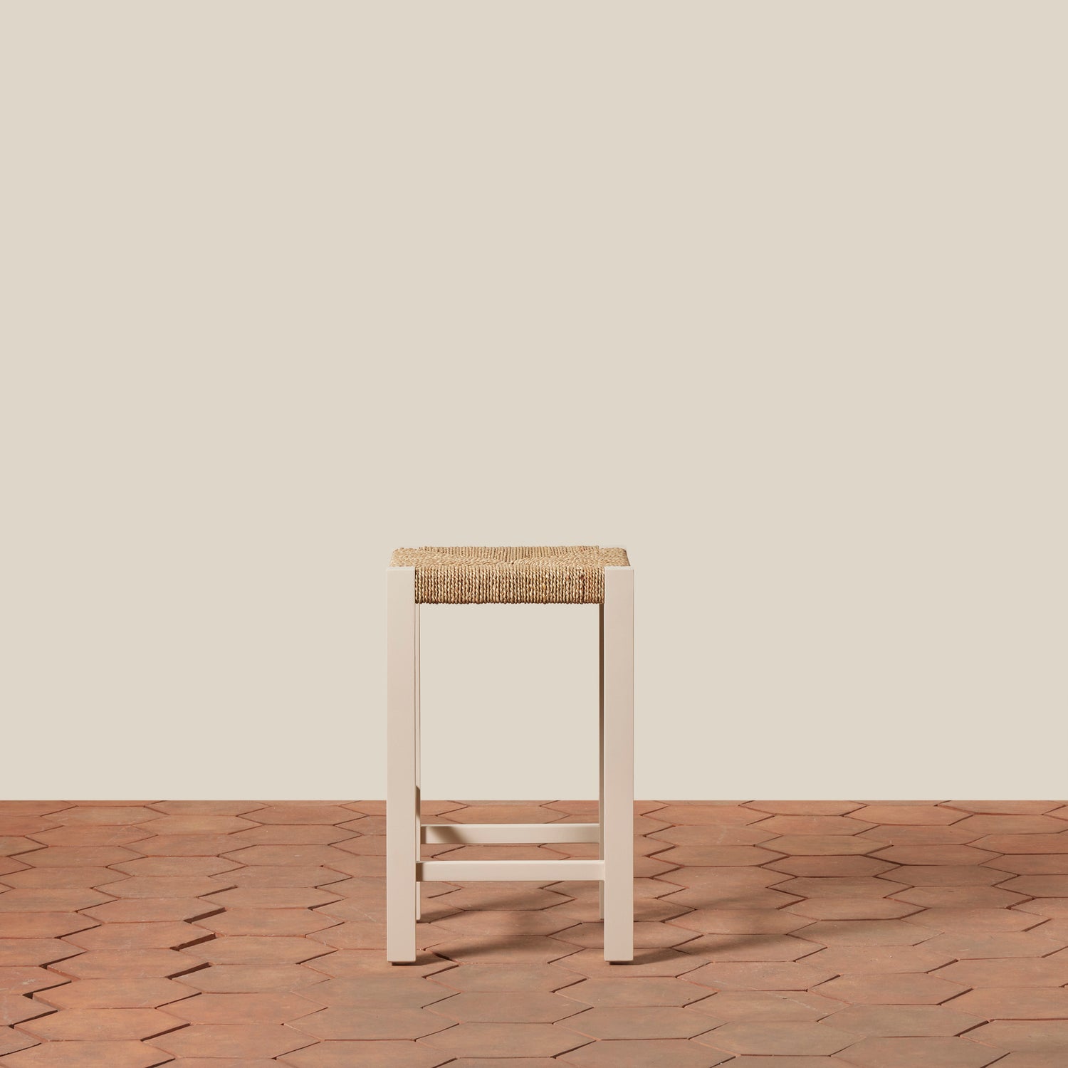 White stool with woven seat on a wooden floor against a beige wall- Number 10