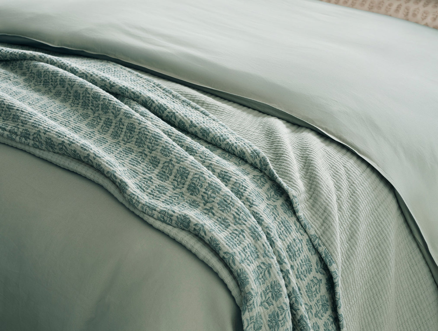 Textured green blanket draped over a bed with a neutral background- Number 5
