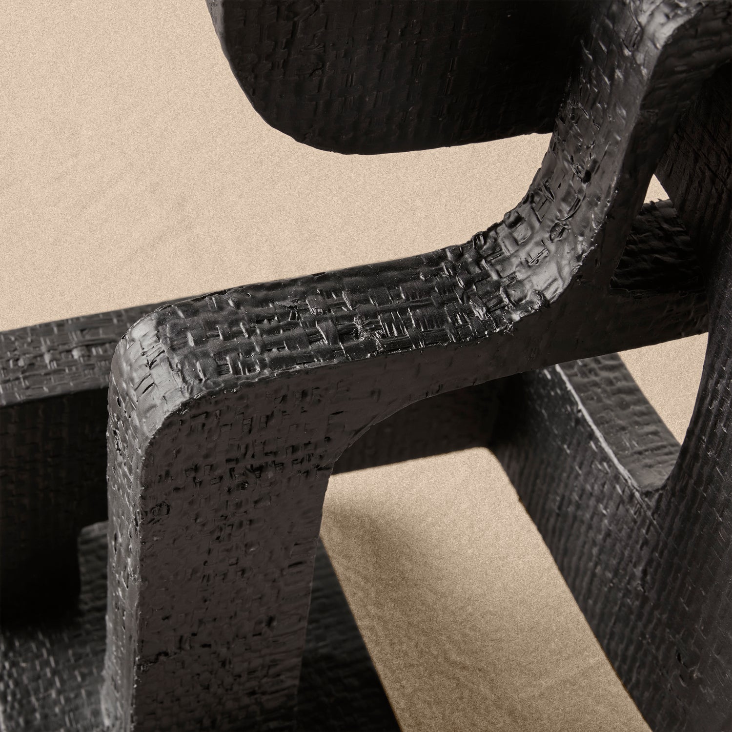 Close-up of a textured black metal sculpture on a beige background- Number 5