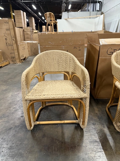 Woven chair in a warehouse setting with cardboard boxes and other furniture.- Number 2