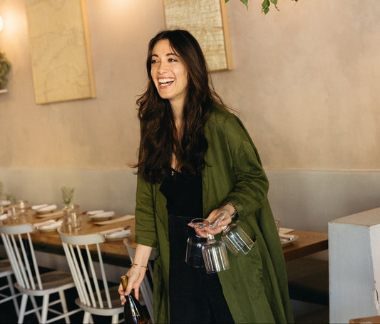 Woman in a green coat holding a bottle in a restaurant setting