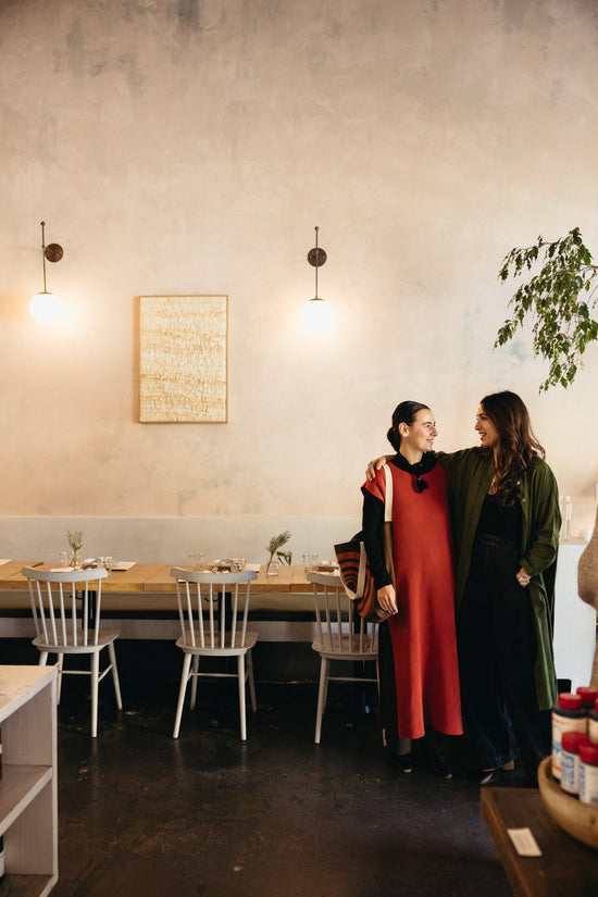 Two women standing in a restaurant with tables and chairs in the background.