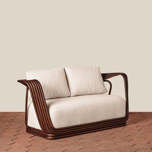 A modern two-seat sofa with textured cream cushions and a curved dark brown wooden frame, set against a solid beige wall and brown herringbone wood floor. - Number 1