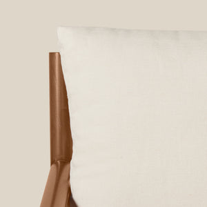 Close-up of a white textured cushion next to a brown leather chair arm against a solid beige background. - Number 6