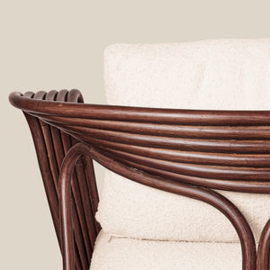 Close-up of a rattan armchair with a curved dark brown frame and a thick cream-colored textured cushion, set against a solid light beige background. - Number 6