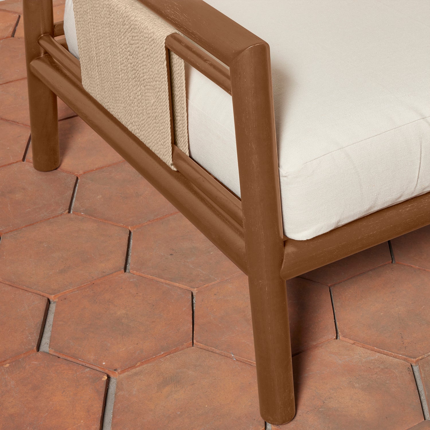 Close-up of an armchair with a brown frame, white cushions, and a beige woven throw, set on terracotta hexagonal tiles.- Number 7